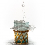Remplissage d'un verre entourrÃ© d'osier avec de l'eau. Le verre dÃ©borde et Ã©clabousse.