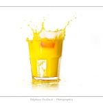 GlaÃ§on qui tombe dans un verre de jus d'orange (boisson jaune) et provoque une Ã©claboussure.
